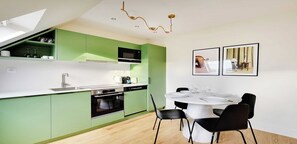 A modern kitchen with green cabinets, a white countertop, and a dining area with a round table and black chairs. - Bright & Stylish Two-Bedroom Apartment with Modern Comforts in Saint-Germain (Paris)