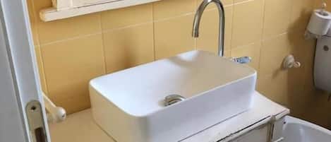 Un bany amb un lavabo blanc, un mirall a la part superior i un vàter.