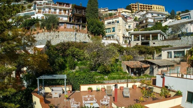A rooftop terrace with outdoor seating and potted plants, surrounded by buildings with balconies and terraces. - Villa Giannina (Taormina)