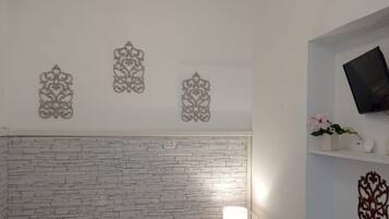 Ein Hotelzimmer mit Ziegelstein-Muster-Kopfstütze, einem Bett mit ordentlich gefalteten weißen Handtüchern, einem Nachttisch mit Lampe und einem an der Wand montierten Fernseher.