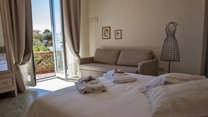 A hotel room with a bed, a sofa, a dress form, and a balcony with curtains. - Villa Giannina (Taormina)