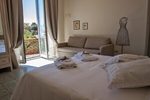 A hotel room with a bed, a sofa, a dress form, and a balcony with curtains.