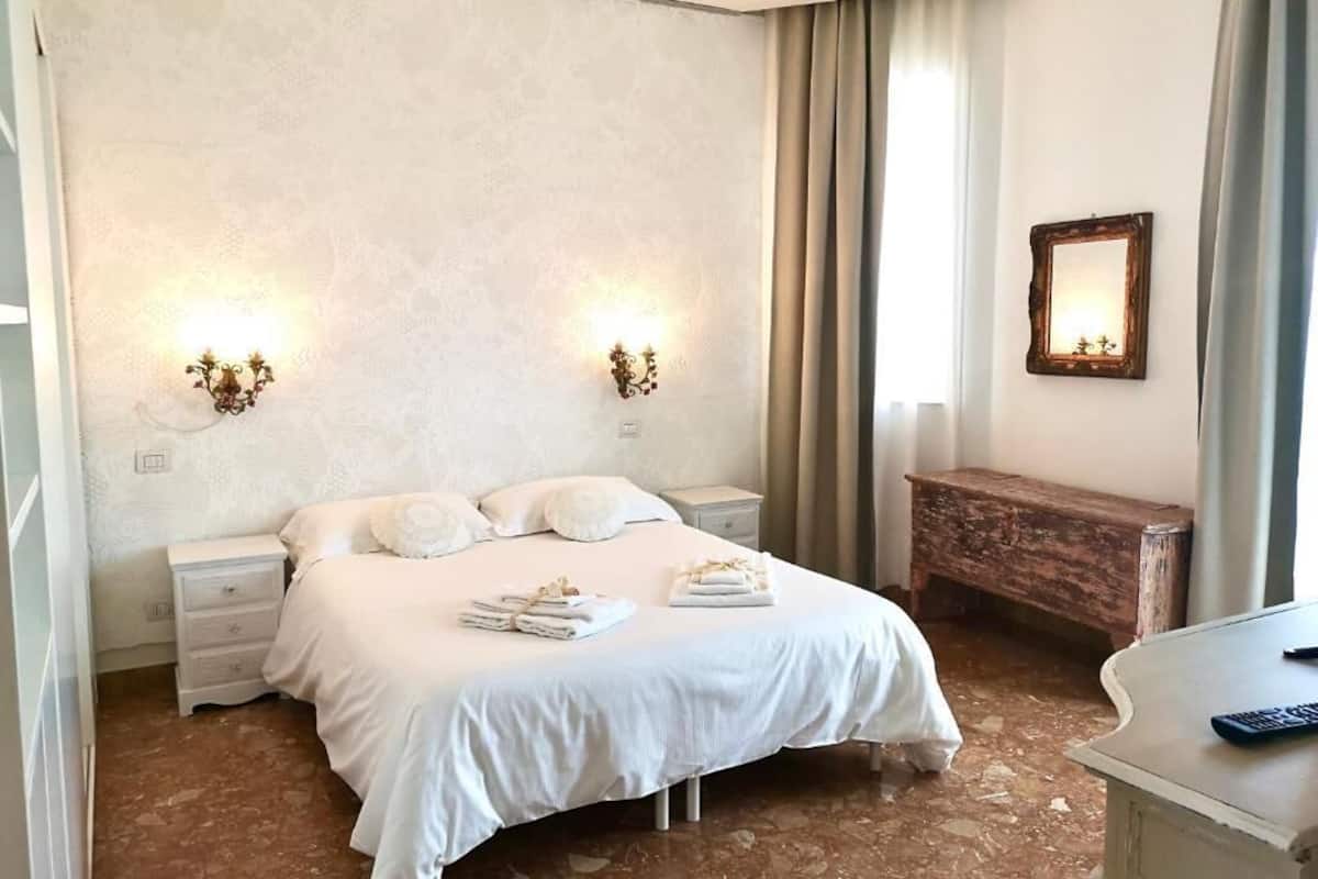 A hotel room with a large bed, two bedside tables, a nightstand, a wooden bench, a desk, and a mirror on the wall.