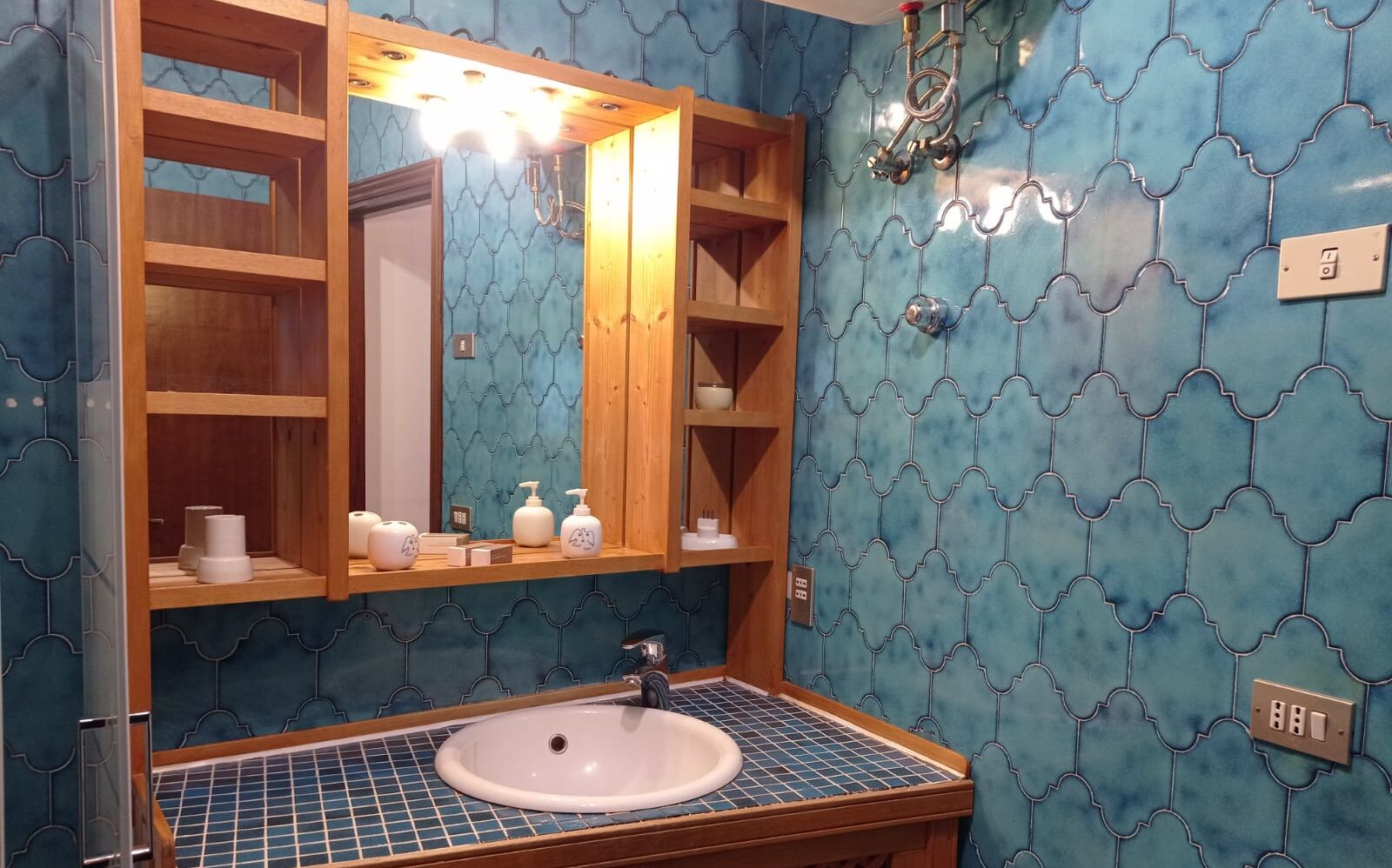 Une salle de bain avec un lavabo, un miroir, des étagères contenant des articles de toilette et un mur à motifs bleus.