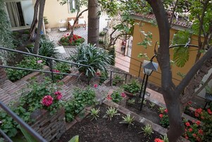 A garden with various plants and flowers, a staircase, and a yellow wall.