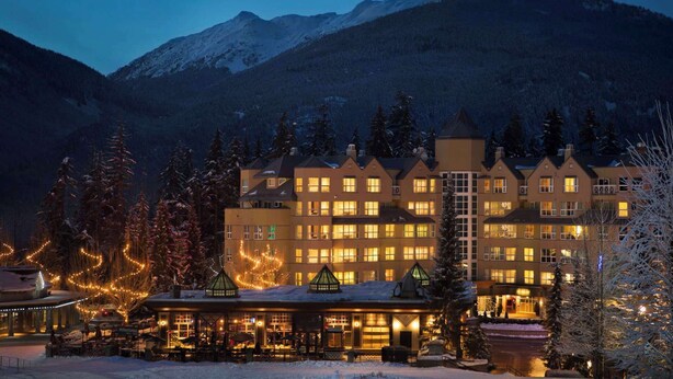A multi-story hotel with a traditional architectural style, featuring a central courtyard with outdoor seating and a snow-covered landscape in the background. - Whistler - Le Chamois - Studio #218 (Whistler)