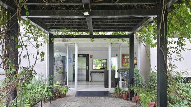 A covered entrance with a tiled floor, potted plants, and a glass door leading to a reception area. - Lux Studio Epic Stay (Gurugram)