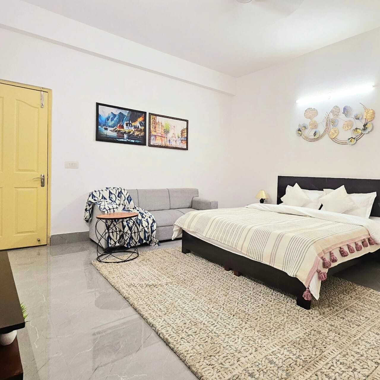 A bedroom with a bed, a sofa, a small table, and a rug. There are two framed pictures on the wall.