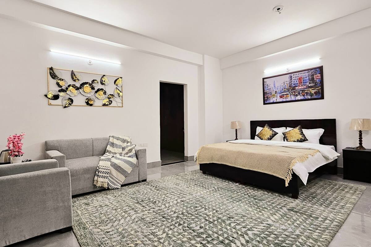 A modern bedroom with a bed, a sofa, a patterned rug, and artwork on the walls.