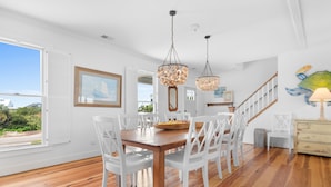 A dining area with a wooden table and white chairs, a chandelier, and a staircase leading to another level. - 6-Bedroom Beach House w/ Private Dock & Pool in Inlet Harbour (Murrells Inlet)