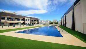 A swimming pool surrounded by artificial grass, with modern buildings in the background.