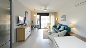 A modern hotel room with a dining area, a sofa, a TV, and a ceiling fan.