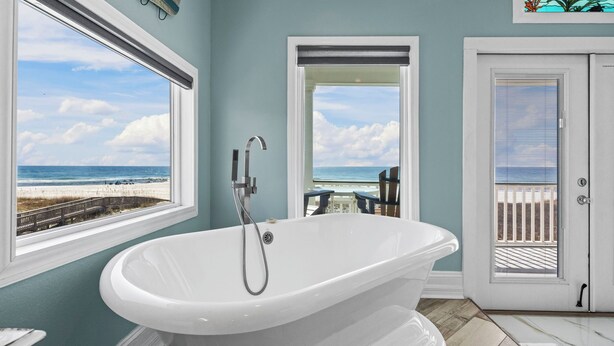 Une salle de bain avec une baignoire sur pieds, une porte avec une fenêtre et une vue sur la plage.