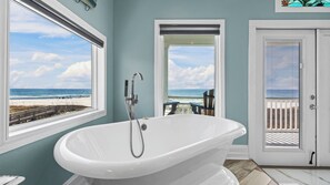 Une salle de bain avec une baignoire sur pieds, une porte avec une fenêtre et une vue sur la plage.