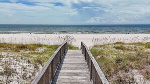 Une promenade en bois mène à une plage de sable où l’herbe y pousse en petites touffes.