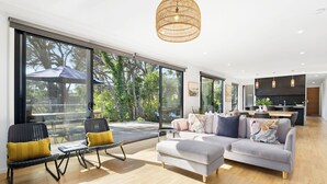A spacious living area with a large sliding glass door leading to a deck, a modern kitchen, and a seating area with a sofa and chairs. - Sublime Sanctuary: 4  BR, 2  BA House in Rye , Sleeps 14 (Rye)