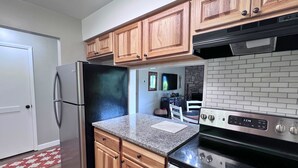 A modern kitchen with wooden cabinets, a stainless steel refrigerator, a granite countertop, and a black stove. - New to our rental program! Cozy and charming 2 bedroom, 1 bath condo (Banner Elk)