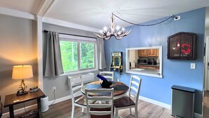 A dining area with a chandelier, a table with chairs, a lamp, and a view of the kitchen through a window. - New to our rental program! Cozy and charming 2 bedroom, 1 bath condo (Banner Elk)