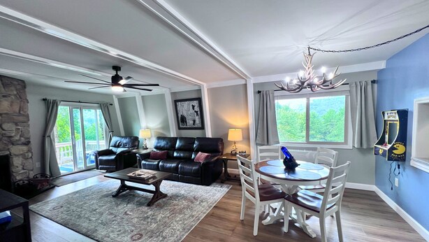 A living room with a fireplace, a dining area with a chandelier, and a view of the outdoors through large windows. - New to our rental program! Cozy and charming 2 bedroom, 1 bath condo (Banner Elk)