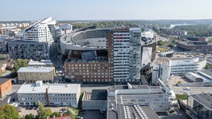 Ein modernes Stadtgebiet mit einer Mischung verschiedener Architekturstile, darunter ein markantes, gebogenes Gebäude und ein mehrstöckiges Haus mit Balkonen.