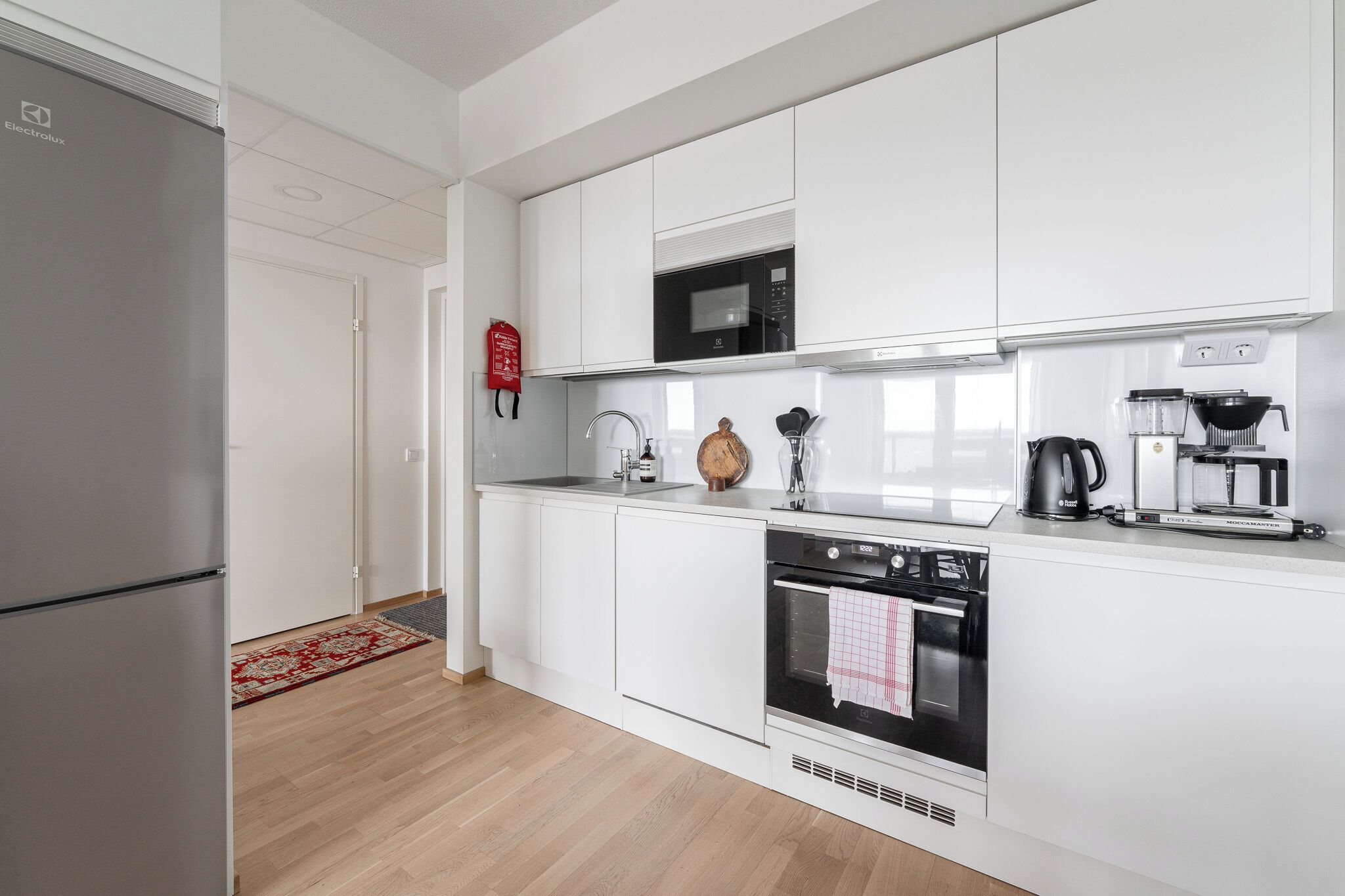 A modern kitchen with white cabinetry, a built-in microwave, a coffee maker, and a kettle.