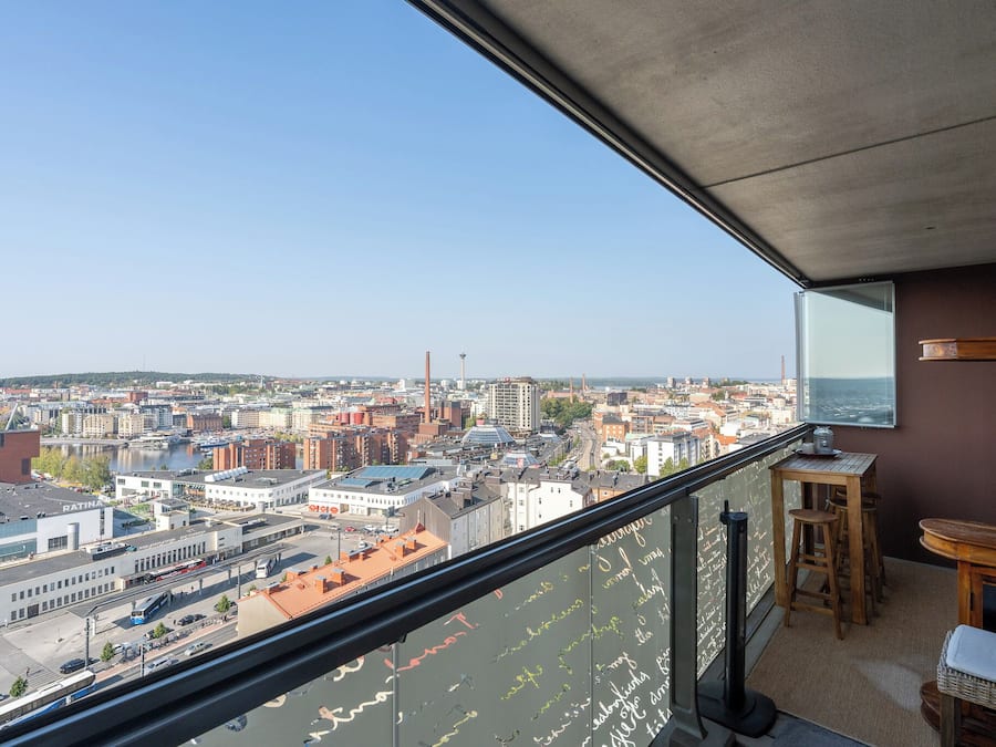 Varanda com vista para a cidade, uma mesa, cadeiras e um quadro negro com anotações.