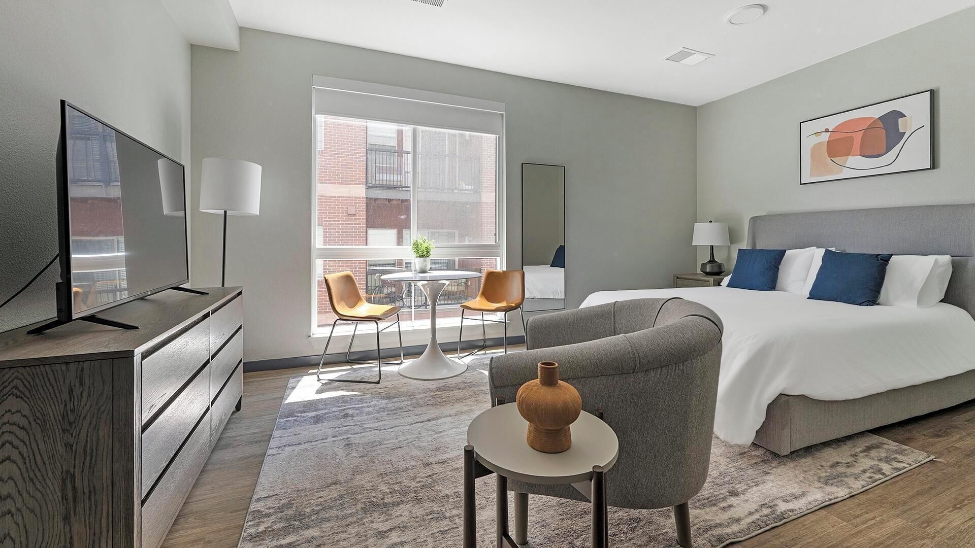 Ein modernes Hotelzimmer mit einem großen Bett, einem Fernseher, einem Schreibtisch und Blick auf die Stadt durch große Fenster.