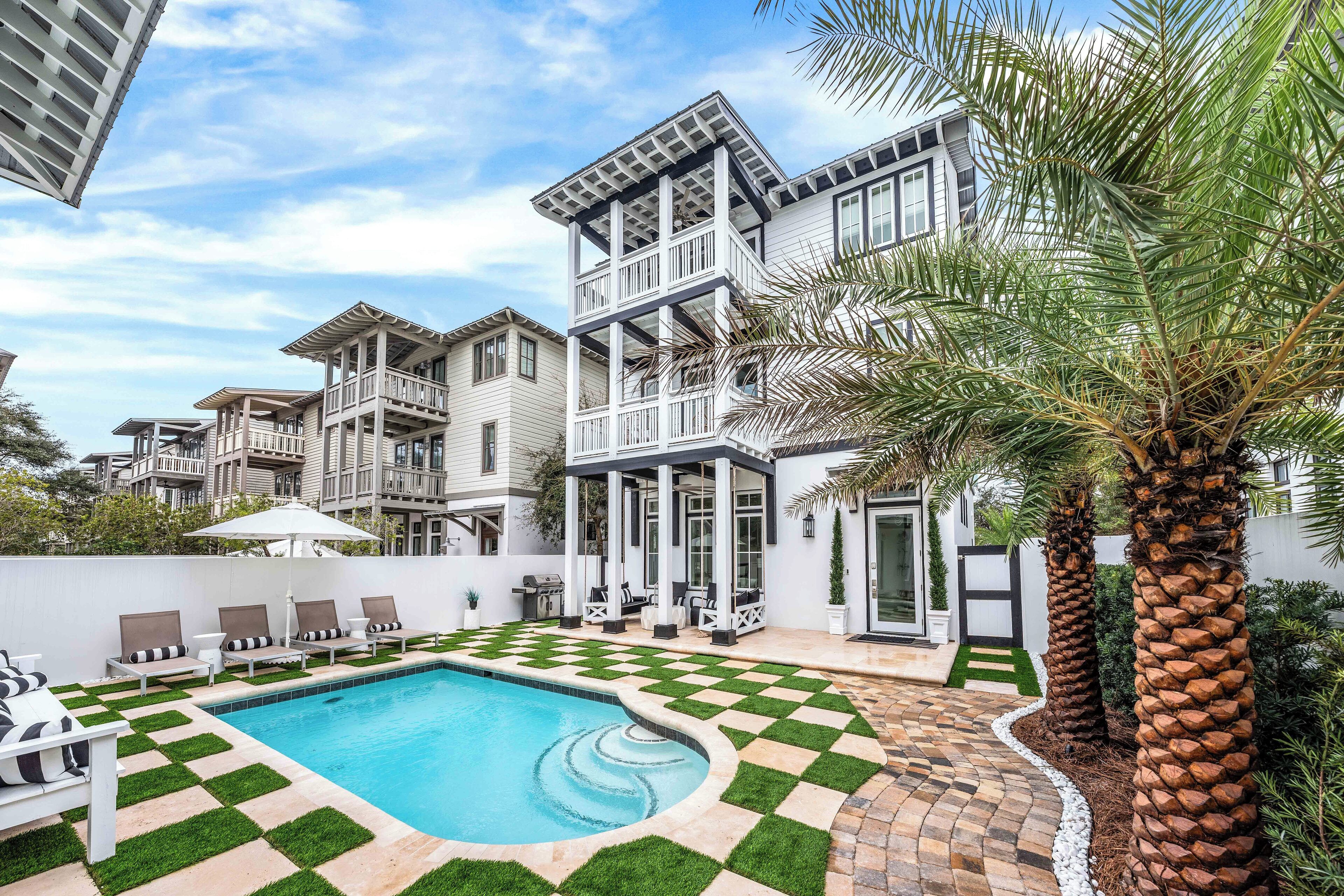 A pool area with a checkered pattern, lounge chairs, and a palm tree.