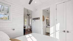 Un dormitorio con cama, ventilador de techo, ventana y puerta con la etiqueta 'BEACH'.