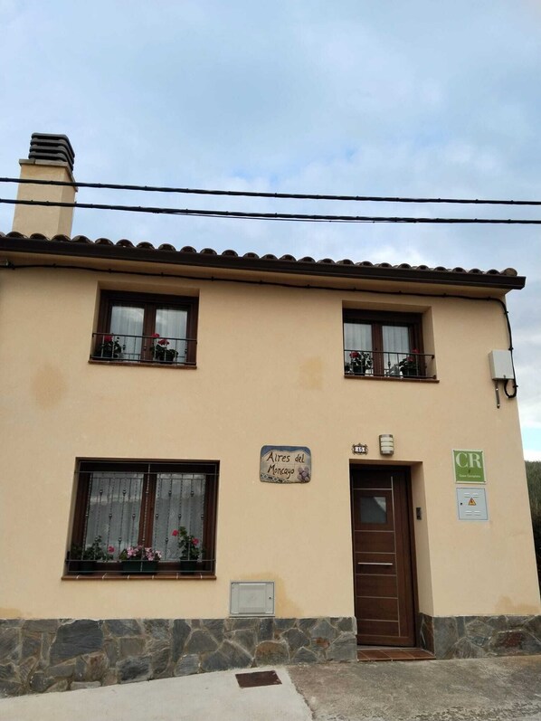 Edificio de dos pisos con cimientos de piedra, una puerta marrón y un cartel que dice "Aires del Moncayo".