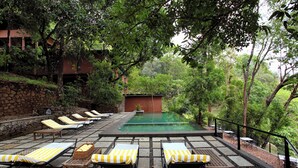 A poolside area with lounge chairs and a small pool, surrounded by trees and a stone wall. - Rainforest  (Chalakudy)