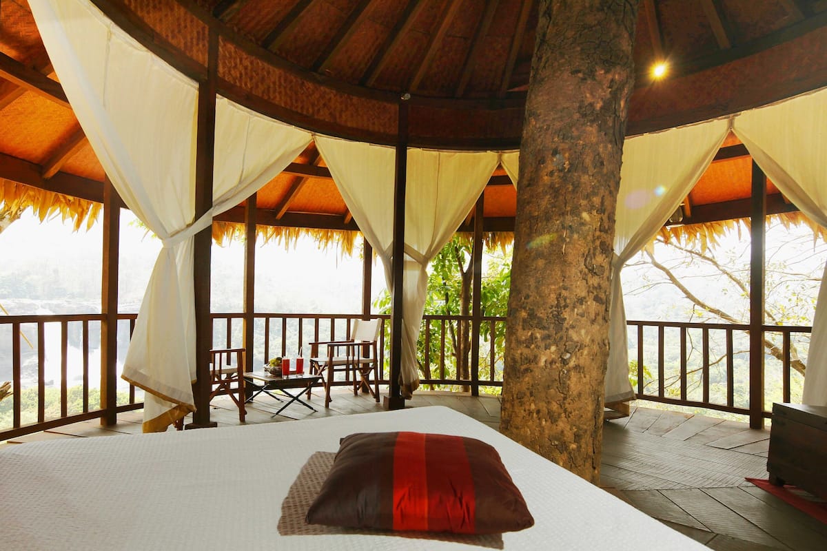 A room with a bed, a table with chairs, and a view of a natural landscape.