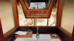 A wooden cabin bathroom with a large sink, wooden shelves, and a window providing a view of trees. - Rainforest  (Chalakudy)