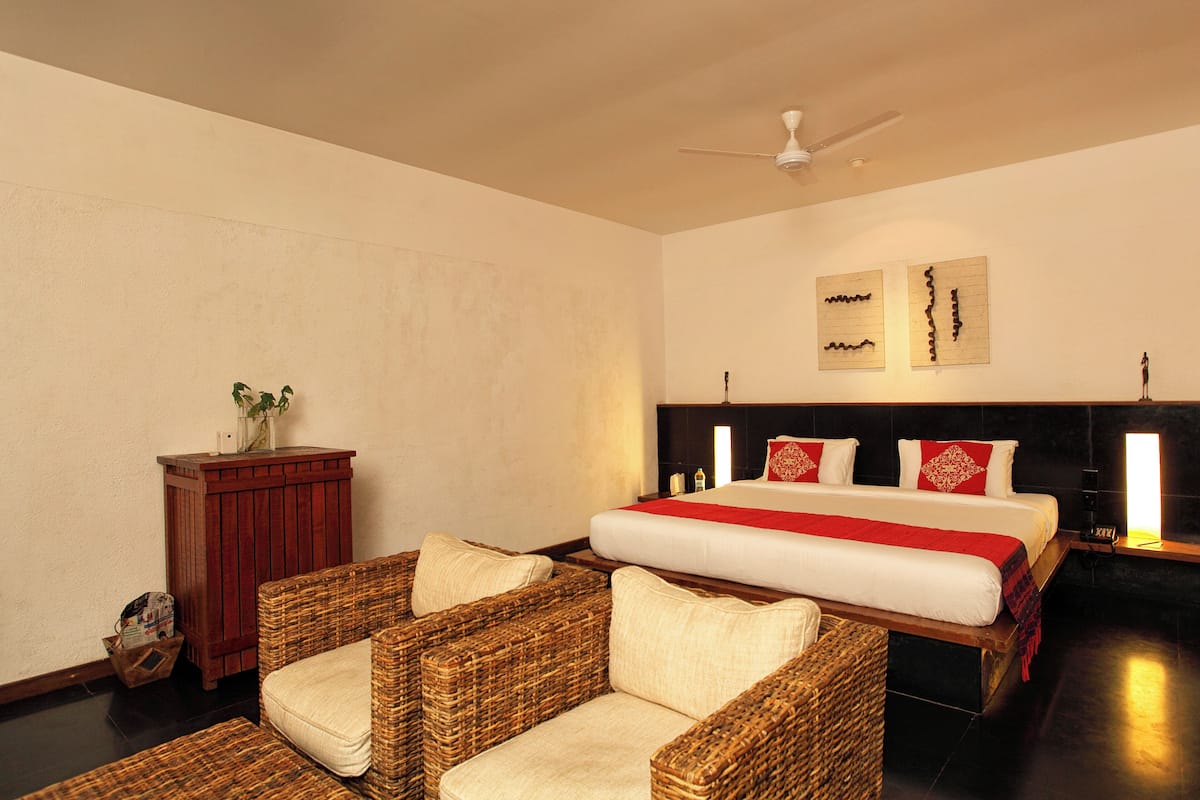 A hotel room with a bed, wicker chairs, a wooden cabinet, and artwork on the wall.