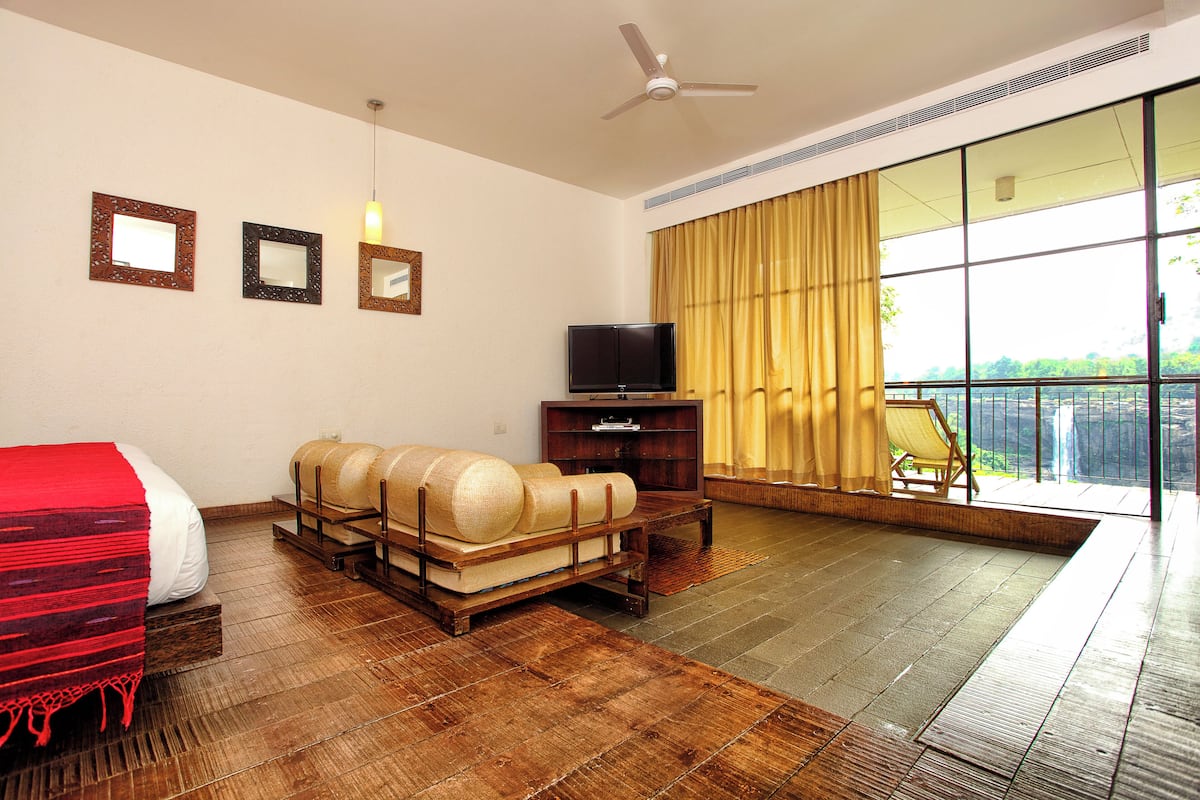 A hotel room with a bed, a sofa, a television, and a large window with curtains.