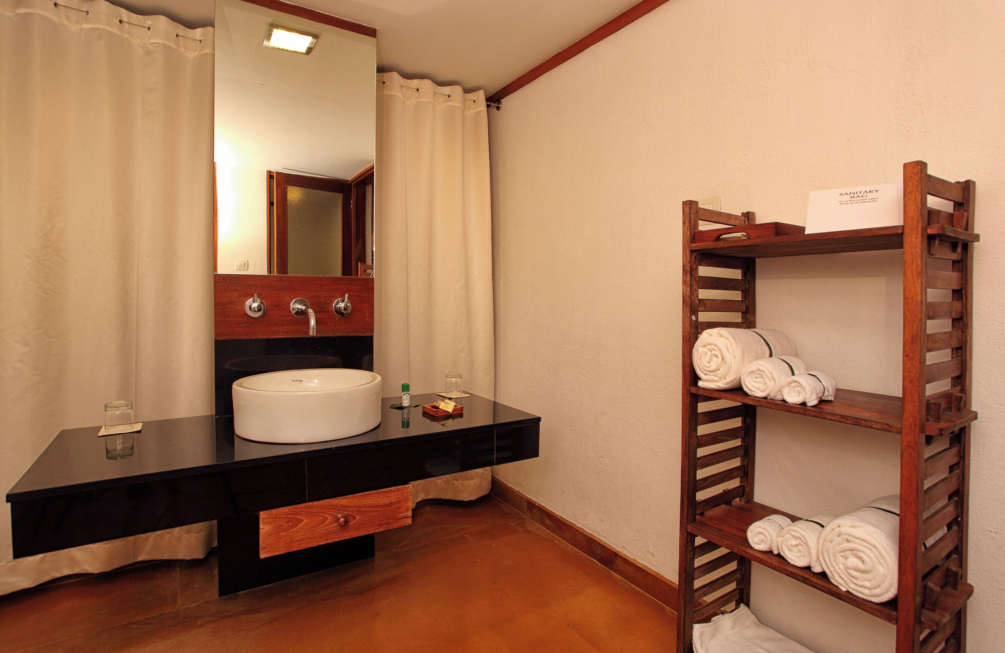 A bathroom with a black countertop, white sink, and a wooden towel rack with towels.