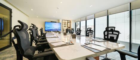 A conference room with a large table, multiple chairs, a television, and a view through large windows.
