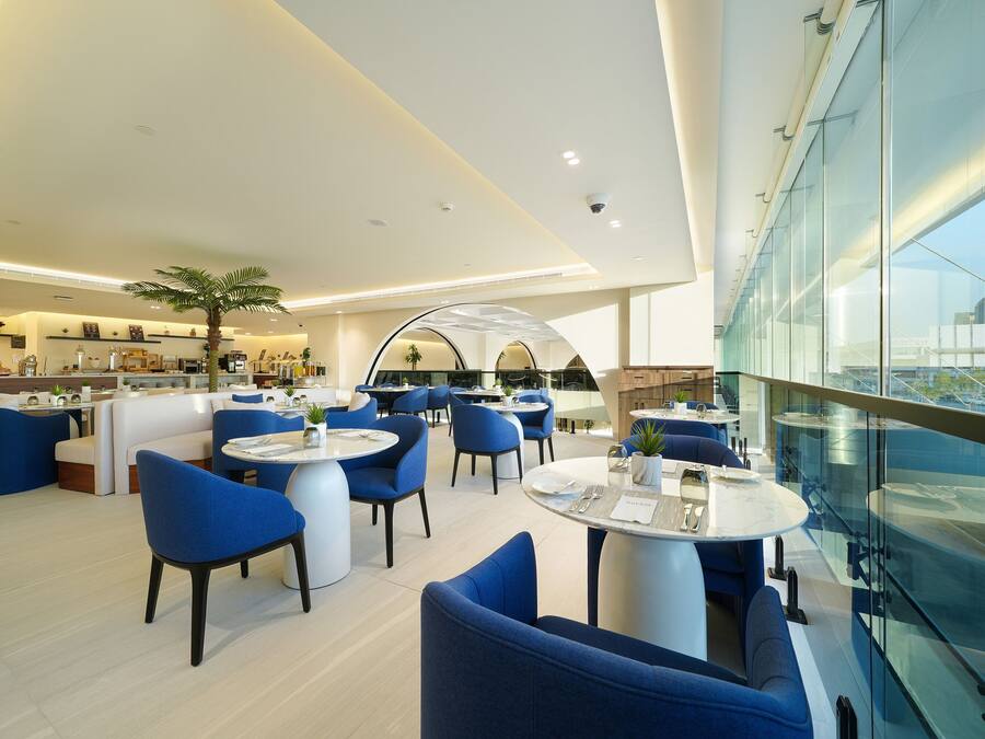 A modern hotel lobby with round tables and blue chairs, a large glass wall, and a view of the city.