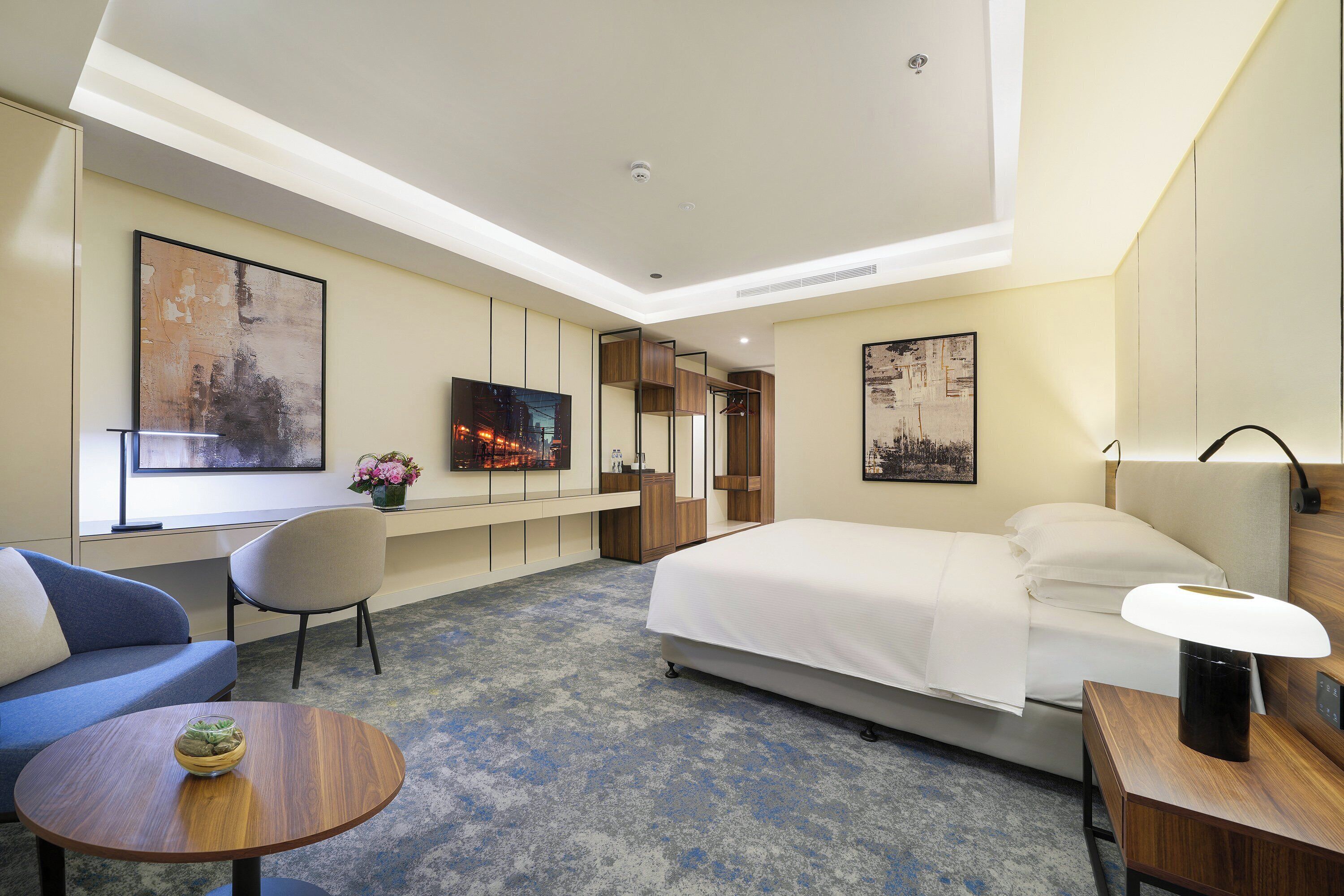 Quarto de hotel moderno com uma cama grande, um sofá, uma mesa redonda e obras de arte nas paredes.
