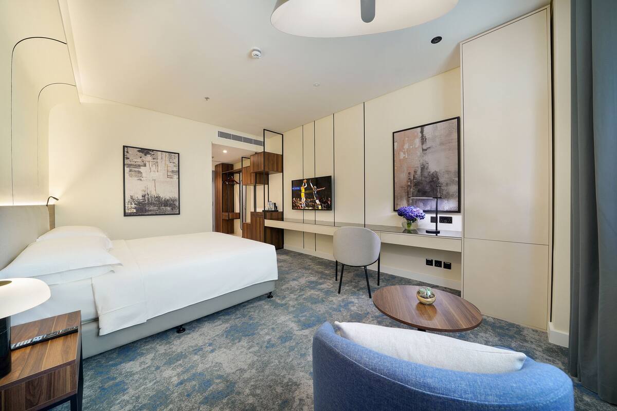 Una camera d'albergo con un letto, una scrivania, una sedia, un tavolo rotondo e opere d'arte alle pareti.