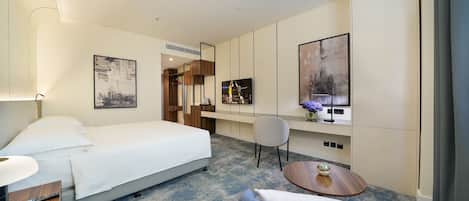 A hotel room with a bed, a desk, a chair, a round table, and artwork on the walls.