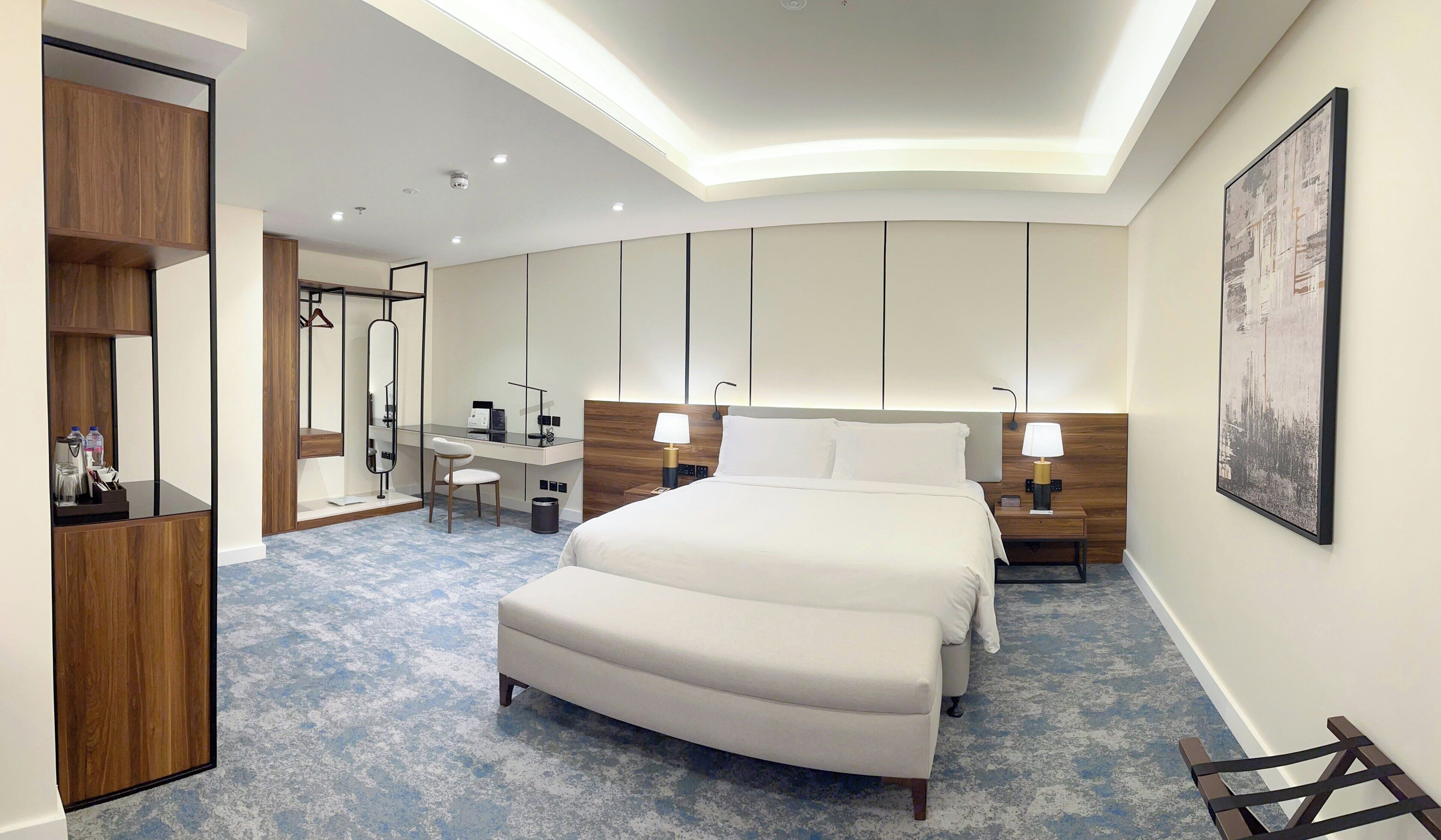 A hotel room with a large bed, a desk, a chair, and a wardrobe.