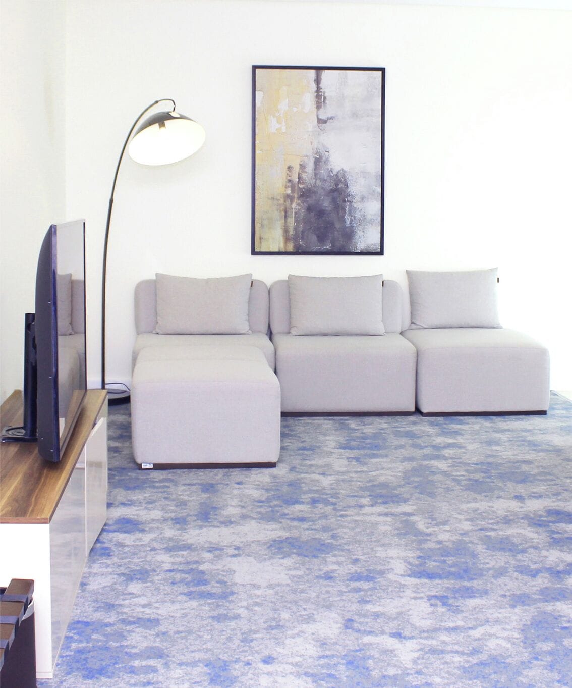 A modern living room with a sectional sofa, a floor lamp, and a framed abstract painting on the wall.