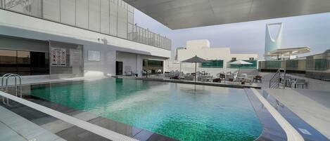 A modern indoor pool with clear water, surrounded by lounge areas and a covered seating area.