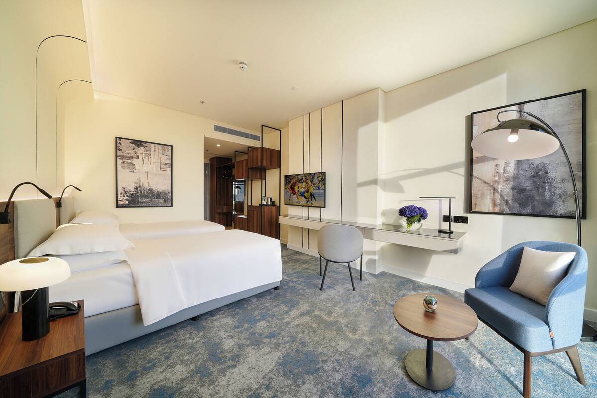 Una camera d'albergo con un letto, una scrivania, una sedia, un tavolino rotondo e opere d'arte alle pareti.