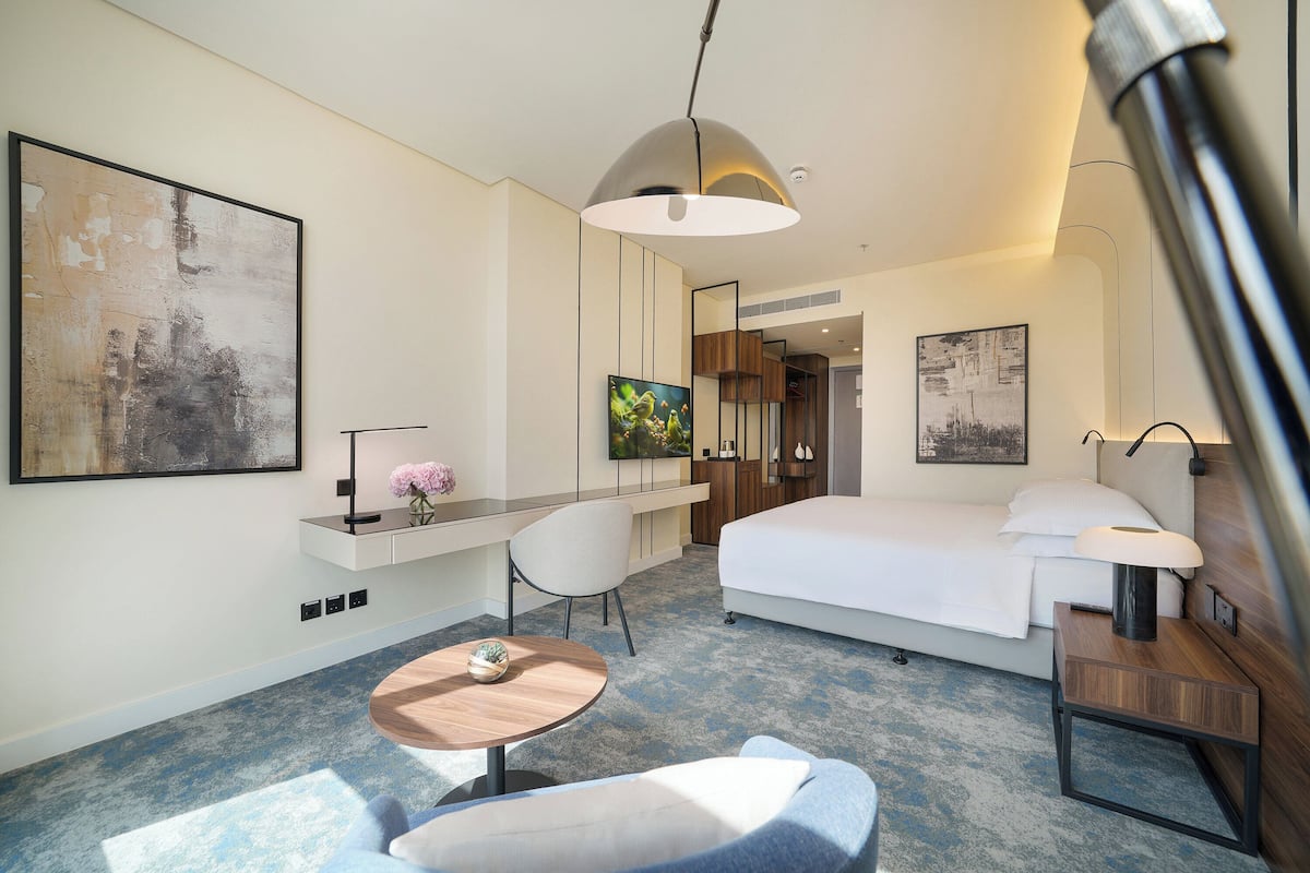 A modern hotel room with a bed, desk, chair, and a small round table.
