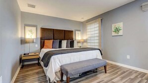 Un dormitorio con cama, banqueta, mesitas de noche y decoración en la pared.