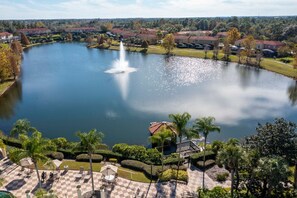 A large lake with a fountain, surrounded by well-maintained gardens and palm trees.