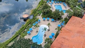 Vista aérea de un complejo turístico con varias piscinas, tumbonas y sombrillas.