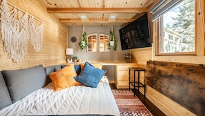 Een knus ogende kamer met een bed, een bureau en een aan de muur bevestigde televisie.